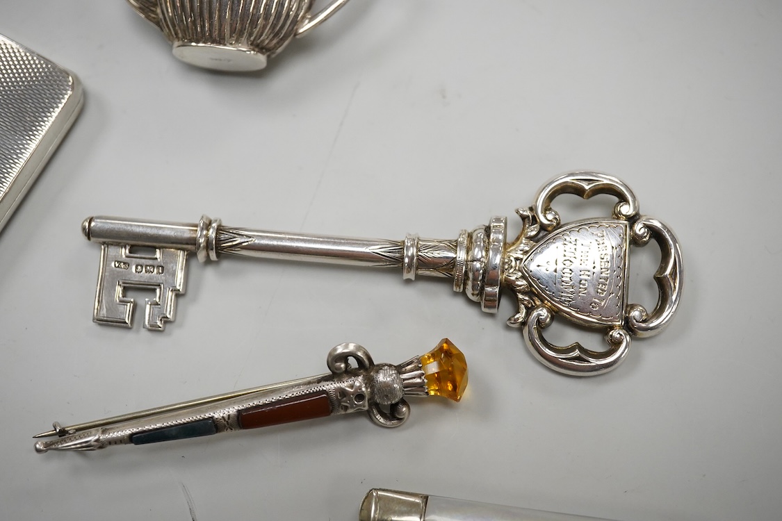 A George V silver presentation key, Vaughton & Sons, Birmingham, 1910, 10.2cm, together with a silver cigarette case, a silver and mother of pearl fruit knife, a miniature 925 demi-fluted teapot and a Scottish hardstone